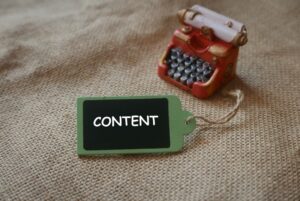 A small toy typewriter and a green tag with the word "CONTENT" written on it, placed on a burlap texture background.