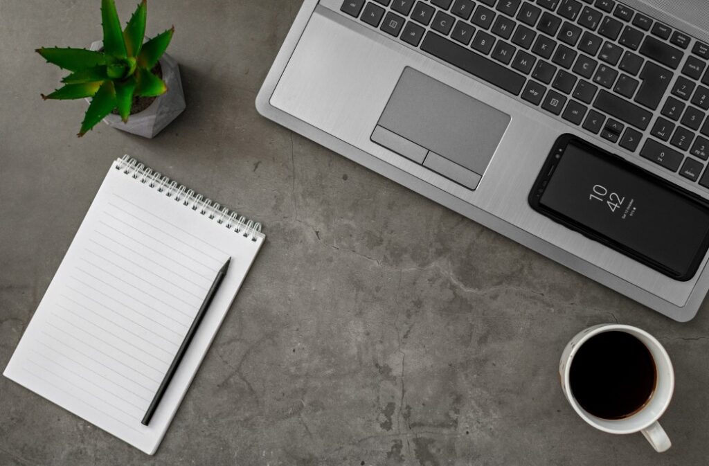 A clean desk space with a laptop, coffee, cell phone and notebook