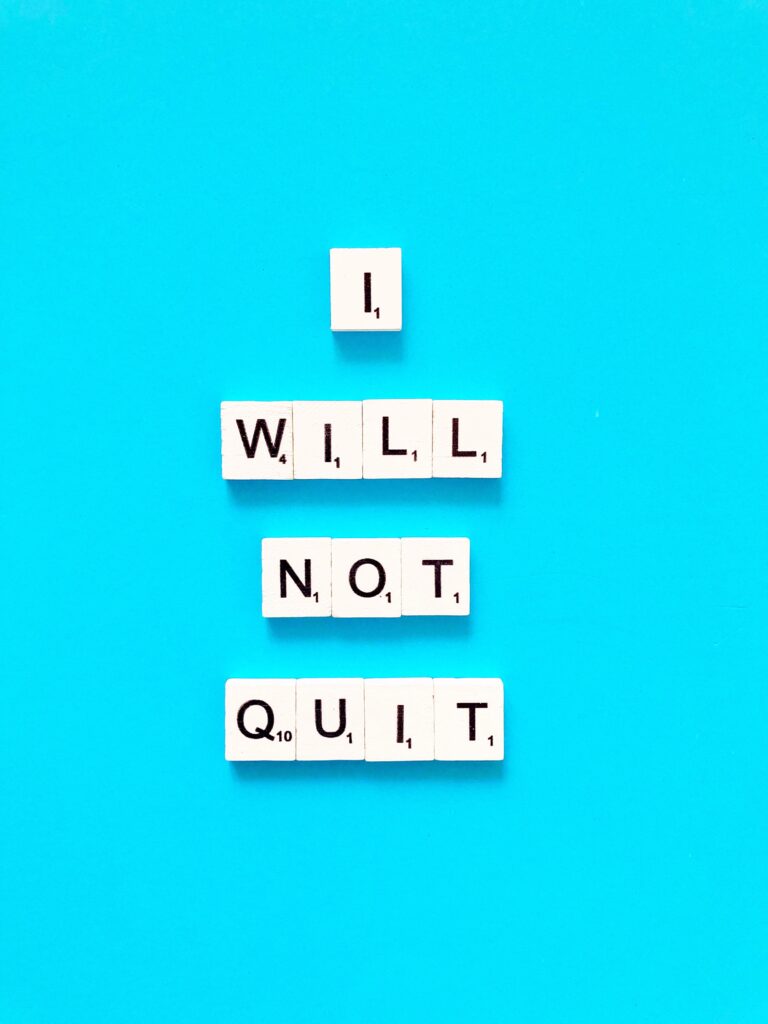 Scrabble letter tiles on a blue background spell out the phrase "I WILL NOT QUIT," capturing the spirit of perseverance and motivation.