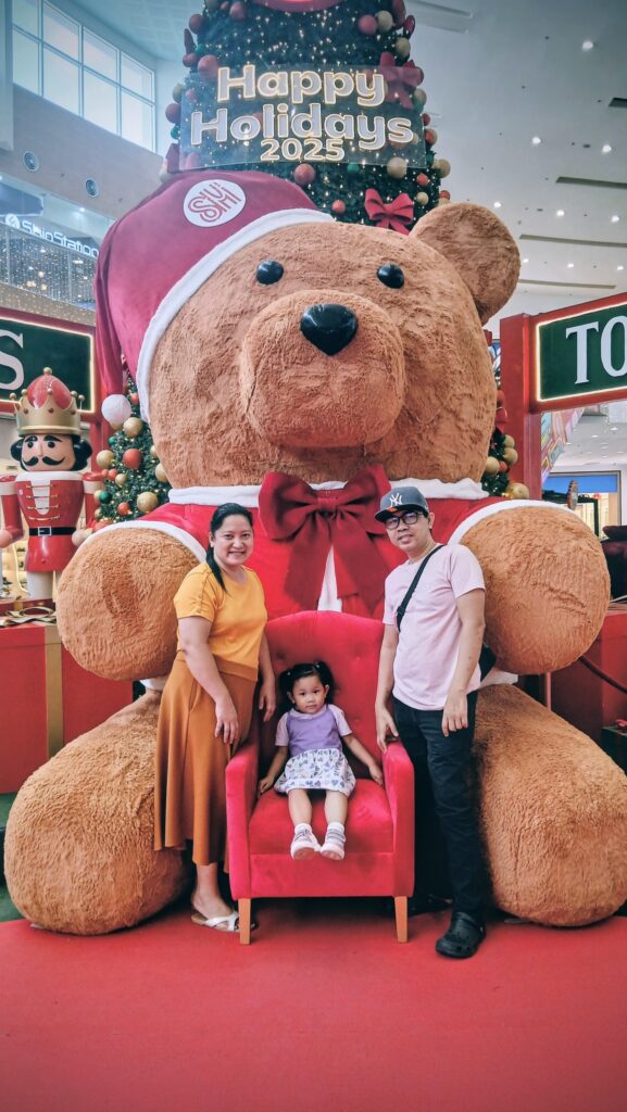 A family poses in front of a giant teddy bear Christmas display at a mall, beneath a "Happy Holidays 2023" sign, capturing a special moment that celebrates the life and legacy of Michael Nicerio.